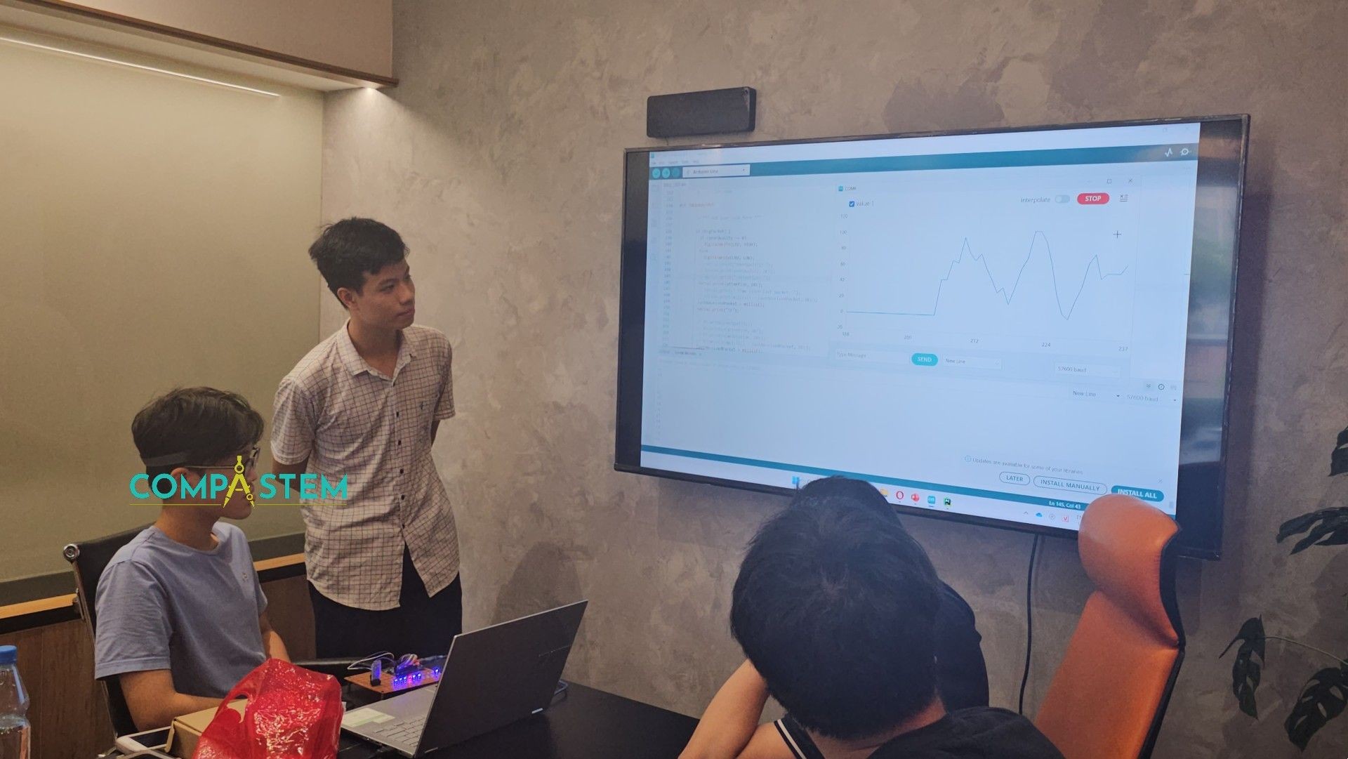 People in a meeting room looking at a screen displaying a graph and code.